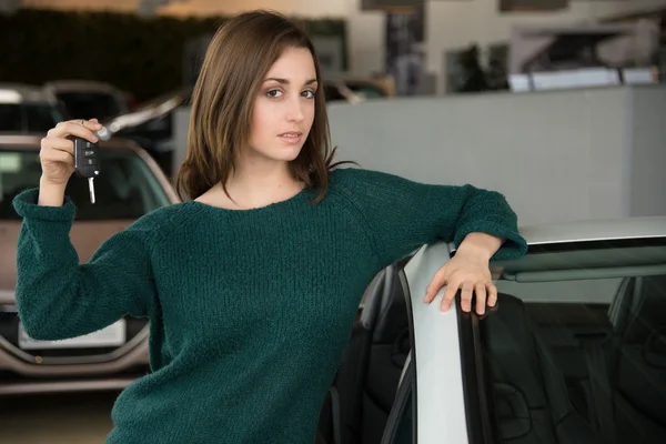 Jeune brune tenant la clé de voiture à l'intérieur concessionnaire automobile — Photo