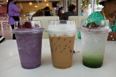Tayland 'da Bangkok, Tayland' da restoran kafeteryasında dinlenen insanların dinlenmesi ve içmesi için gazoz ve yabanmersinli meyve suyu ve plastik cam bardakta buzlu kahve.