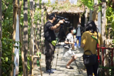 Taylandlı erkeklerin muhabirleri, Bangkok, Tayland 'daki Nonthaburi şehrindeki bahçe parkındaki organik çiftçi sokak festivali festivalinin canlı yayını için dijital kamera görüntülerini kullanıyorlar.