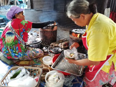 Taylandlı yaşlı kadın ve kız kardeşler 18 Kasım 2020 'de Trang, Tayland' da yerel pazarda geleneksel Tayland tatlıları veya Tayland hindistancevizli krep kekleri satarak tatlı yemek pişirirler.