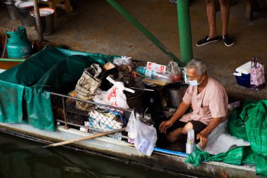Taylandlı yabancı gezginler 20 Mart 2022 'de Nonthaburi, Tayland' da yerel Wat Takhian Yüzen Pazarı 'ndaki ahşap teknedeki bakkaldan alışveriş yiyecek içecek ürünlerini ziyaret ediyorlar.