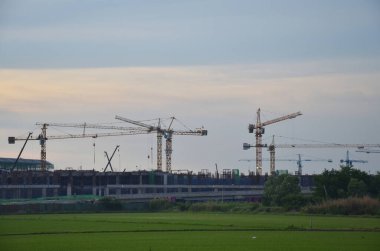 Asian labor people and thai labour worker use machine and heavy machinery working builder railway track electric skytrain at construction site with paddy rice field at sunrise dawn in Bangkok Thailand