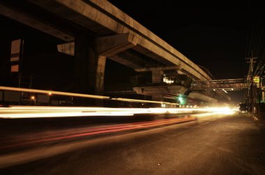 Gece vakti Thailand, Nonthaburi 'deki Bang Bua Thong' da trafik yolunda ve MRT trenin mor renkli tren hattında bulanık ışık hareketi