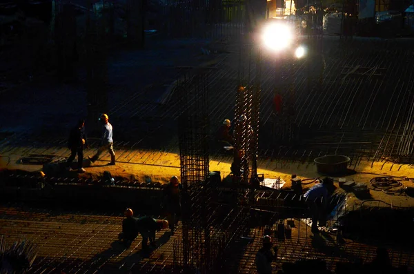 Asian labor people and thai labour worker knitting metal rods bars into framework reinforcement for concrete pouring for working structure building at construction site night time in Bangkok, Thailand