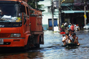 Taylandlı doğal afet kurbanları, 20 Ekim 2011 'de Nonthaburi Tayland' da kırsal kesimde su taşkınları ve kurtarma çalışmalarına yardım ederken, su taşkınları caddesinde suda yüzen araçları kullanıyorlar.