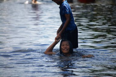 20 Ekim 2011 'de Nonthaburi, Tayland' da kırsal Bang Bua Tanga başkentinde su taşkınları ve sel baskını yolunda yüzerken Taylandlı kız kardeşler ve arkadaşları sokakta yüzüyorlar.