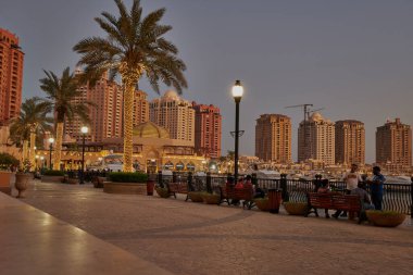 İnci Doha 'da Porto Arabistan, Katar' da kış günbatımı çekimleri arka planda ufuk çizgisi olan gezinti güvertesinde yürüyen ve oturan insanları gösteriyor.