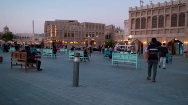 Souq Waqif, Doha, Katar ana caddesinde gün batımında geleneksel Arap Tekstil Dükkanı, Kafeler, yerliler ve yürüyen ziyaretçileri gösteriyor. Katar Corona virüs salgınından sonra yeniden açıldı 