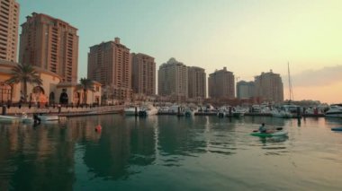 Peral Doha 'da Porto Arabistan marinası, Katar' da gün batımı, rıhtım tekneleri ve yatları, Arap Körfezi 'nde kano eğitimi ve arkadaki konut binalarını gösteriyor. 