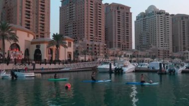 Peral Doha 'da Porto Arabistan marinası, Katar' da gün batımı çekimleri rıhtım tekneleri ve yatları, Arap Körfezi 'nde kano eğitimi ve arka plandaki konut binalarını gösteriyor.