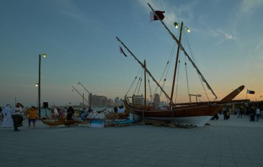 Doha Katar 'da düzenlenen 11. Geleneksel Dhow Festivali, Katar Bayrakları' nın yerel halk ve ziyaretçilerle birlikte sergilendiği gün batımı çekimini gösteriyor.
