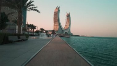 Lusail Corniche, Lusail 'deki marinada, Katar' da gün batımı çekimleri fıskiyeyi gösteriyor, insanlar arka planda ufuk çizgisiyle geziniyor.