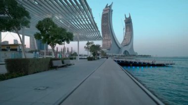 Lusail Corniche, Lusail 'deki marinada, Katar' da gün batımı çekimleri fıskiyeyi gösteriyor, insanlar arka planda ufuk çizgisiyle geziniyor.