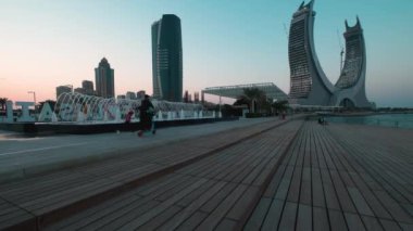 Lusail Corniche, Lusail 'deki marinada, Katar' da gün batımı çekimleri fıskiyeyi gösteriyor, insanlar arka planda ufuk çizgisiyle geziniyor.