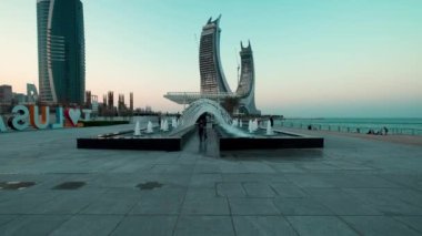 Lusail Corniche Lusail City 'de, Katar' da marinada gün batımı çekimleri fıskiyeyi gösteriyor, insanlar arka planda ufuk çizgisiyle geziniyor.