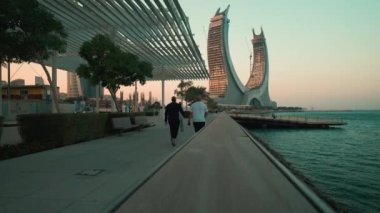 Lusail Corniche, Lusail City 'deki marinada, Katar' da gün batımı çekimleri fıskiyeyi gösteriyor, insanlar arka planda ufuk çizgisiyle geziniyor.