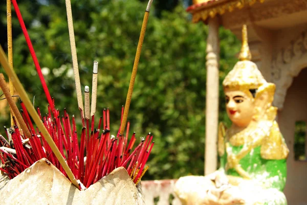 Rode wierook stokjes tegenover een boeddhist standbeeld — Stockfoto