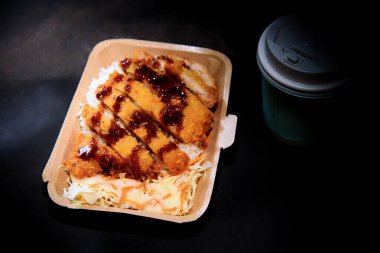 Tonkatsu Pork Rice Japon sosu siyah arka planda bir fincan sıcak kahveyle bir kutuya döküldü.