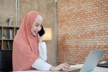 İslami kadın islami bir iş kadınının cep telefonu iletişimi ve mutlu bir gülümseme ile konuştuğu güzel bir iş kadını. Çünkü internet sitesi dizüstü bilgisayar, modern yaşam tarzı, e-ticaret mesleği.