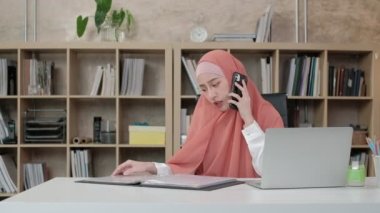 Güzel iş kadını, İslami kadın kişi oturuyor ve cep telefonu iletişimiyle meşgul çünkü online düzen dizüstü bilgisayar, modern çalışma tarzı internet, e-ticaret mesleği.