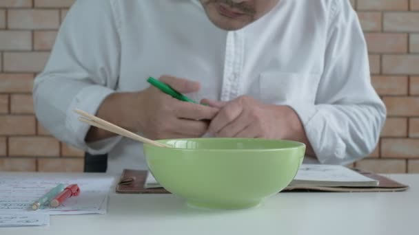 Trabajador Masculino Asiático Lee Libro Citas Mientras Come Fideos Instantáneos — Vídeo de stock