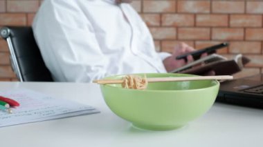 Asyalı erkek işçiler yemek molasında beyaz kasede yemek çubuklarıyla yemek yerken randevu kitabı okurlar. Yemek molası sırasında, alelacele sağlıksız bir yaşam tarzı..