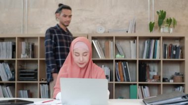 İslamcı çiftler olan iki genç girişimci, e-ticaret sektöründe gülümseyerek çalışmanın başarısı hakkında konuşuyor. Küçük bir ofiste internet üzerinden çevrimiçi iletişim kurmak için laptop kullan.