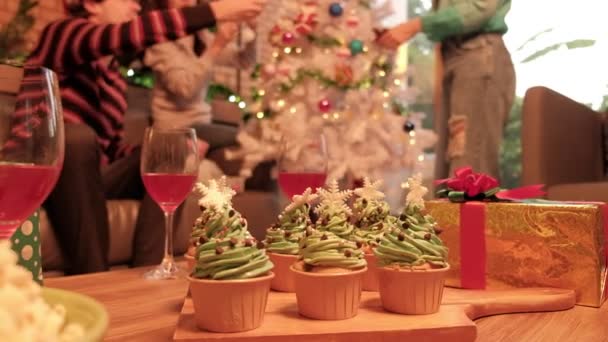 クリスマスツリーを飾る家族や友人の前でカップケーキ ワインドリンク ギフト およびその他の装飾品の選択的な焦点は お祝いパーティーは自宅のリビングルームで準備し 新年の祭り — ストック動画