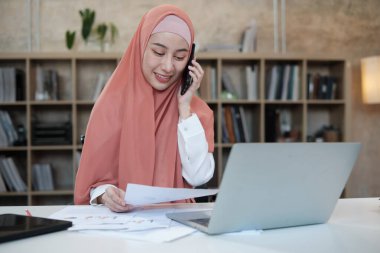 İslami kadın islami bir iş kadınının cep telefonu iletişimi ve mutlu bir gülümseme ile konuştuğu güzel bir iş kadını. Çünkü internet sitesi dizüstü bilgisayar, modern yaşam tarzı, e-ticaret mesleği.