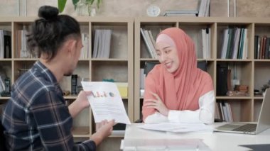 Güzel bir İslami patrona e-ticaret grafikleri ile iş dünyasının başarısı için sunum ve tartışma yapan, küçük bir ofiste masa başı işi yapan bir erkek işçi.