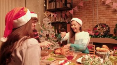 Arkadaşlar, özel yemeklerle dolu bir masada, süslerle süslenmiş, Noel festivali ve yeni yıl kutlamalarıyla süslenmiş, kızarmış hindiyi kesen genç bir kadının tadını çıkarıyorlar..