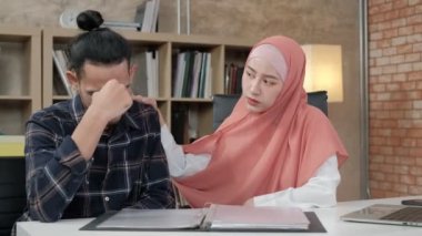 İslami bir kişi olan genç bir bayan girişimci iş ortağı, erkek meslektaşını küçük iş yerinde, e-ticaret ofisinde üzgün ve stresli olmaktan teşvik ediyor ve rahatlatıyor..