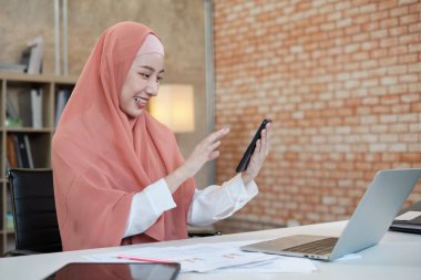 İslami kadın islami bir iş kadınının cep telefonu iletişimi ve mutlu bir gülümseme ile konuştuğu güzel bir iş kadını. Çünkü internet sitesi dizüstü bilgisayar, modern yaşam tarzı, e-ticaret mesleği.