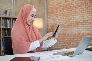 İslami kadın islami bir iş kadınının cep telefonu iletişimi ve mutlu bir gülümseme ile konuştuğu güzel bir iş kadını. Çünkü internet sitesi dizüstü bilgisayar, modern yaşam tarzı, e-ticaret mesleği.
