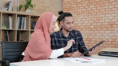 İslamcı çiftler olan iki genç girişimci, e-ticaret sektöründe gülümseyerek çalışmanın başarısı hakkında konuşuyor. Küçük bir ofiste internet üzerinden çevrimiçi iletişim kurmak için dijital tablet kullan.