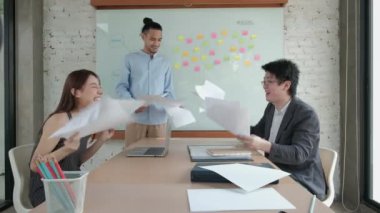 Mutlu Asyalı profesyonel ofis ekibi neşeli ve şirket işinin başarısını kutluyor. Kağıtları bir araya getirip toplantı odasında renkli yapışkan notlarla uçtular..