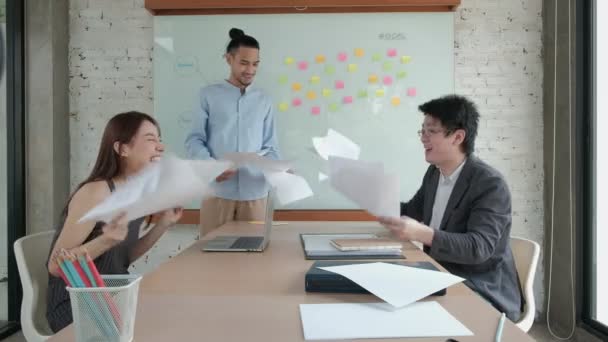快乐的亚洲专业办公室团队是快乐的 庆祝公司业务的成功 他们把文件扔在一起 在会议室里飞来飞去 桌上挂着彩色的粘贴字条 — 图库视频影像