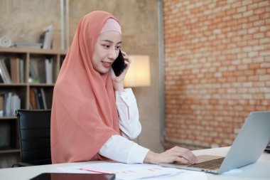 İslami kadın islami bir iş kadınının cep telefonu iletişimi ve mutlu bir gülümseme ile konuştuğu güzel bir iş kadını. Çünkü internet sitesi dizüstü bilgisayar, modern yaşam tarzı, e-ticaret mesleği.