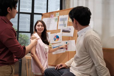 Kadın işçi, Asyalı iş arkadaşlarına iş yerindeki mali tabloyu sunar ve açıklar. Üç iş arkadaşı iş planı stratejisi ve pazarlama raporunu tartışıyor.