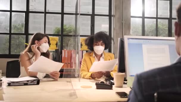 新しい通常オフィスで働くフェイスマスクを持つ2人の女性同僚チーム Covid 19クリアパーティション 事業場オフィス パンデミック健康のための社会的距離 病気の予防による保護 — ストック動画