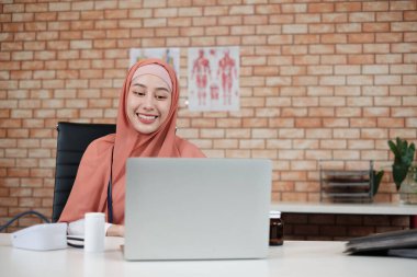 Güzel bir kadın doktorun portresi, üniformalı güzel bir Müslüman steteskoplu, gülümseyen ve hastanenin kliniğinde dizüstü bilgisayarla çalışan. Profesyonel tedavide uzmanlaşmış bir kişi.