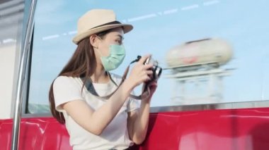 Yüz maskeli güzel Asyalı kadın turist kırmızı koltukta oturur, trenle seyahat eder, fotoğraf çeker, banliyöde seyahat eder, tren yoluyla yolcu yaşamının tadını çıkarır, iyi yolculuklar..