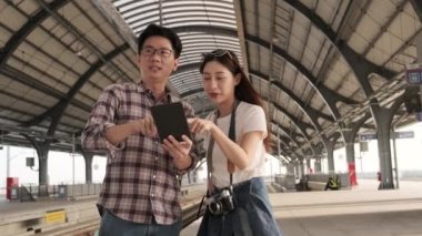 Genç bir çift Asyalı turist bilgi arıyor, Tayland 'daki bir tren istasyonunun kavşağında tablet haritasıyla seyahat yerlerini buluyor, yolcu gezisi yaşam tarzı, günlük ulaşım, seyahat tatili. 