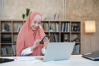 İslami kadın islami bir iş kadınının cep telefonu iletişimi ve mutlu bir gülümseme ile konuştuğu güzel bir iş kadını. Çünkü internet sitesi dizüstü bilgisayar, modern yaşam tarzı, e-ticaret mesleği.