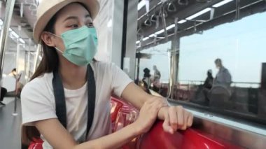 Yüz maskeli güzel Asyalı kadın turist kırmızı koltukta oturur, trenle seyahat eder, fotoğraf çeker, banliyöde seyahat eder, tren yoluyla yolcu yaşamının tadını çıkarır, iyi yolculuklar..