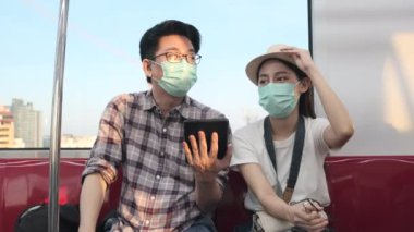 Genç yüz maskesi takan birkaç Asyalı turist bilgi arıyor, bir tren kulübesinde seyahat yerlerini tablet haritasıyla buluyorlar, yolcu gezisi yaşam tarzı, günlük ulaşım, Tayland seyahati.