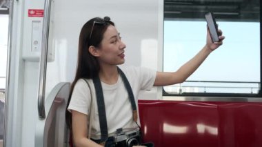 Genç ve güzel Asyalı kadın turist çevrimiçi sohbet, cep telefonu görüntülü konuşma, giriş ve sosyal medya paylaşımı, şehir içi seyahat, yolcu yaşam tarzı, iyi yolculuklar..