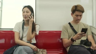 Kameralı güzel Asyalı bayan turist kırmızı koltukta oturur, gökyüzü treniyle seyahat eder, şehir manzarasında taşınırken cep telefonuyla konuşur, tren yoluyla şehir yolcusu yaşam tarzı, iyi yolculuklar..