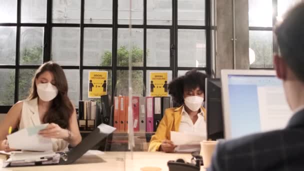 新しい通常オフィスで働くフェイスマスクを持つ2人の女性同僚チーム Covid 19クリアパーティション 事業場オフィス パンデミック健康のための社会的距離 病気の予防による保護 — ストック動画