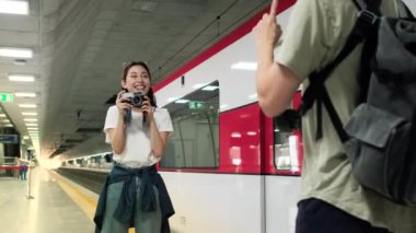 Genç ve güzel bir Asyalı kadın turist, erkek arkadaşıyla fotoğraf çekiyor, tren istasyonunda gülümsüyor ve eğleniyor, metro yolculuğuyla mutlu bir hayat sürüyor..